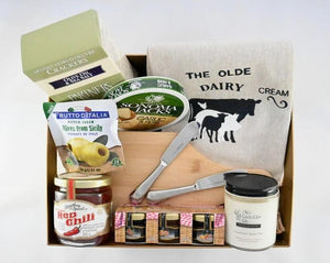 Happy Home Basket with a selection of products including charcuterie board and spreaders, jams and jellies, a candle, and kitchen towel.