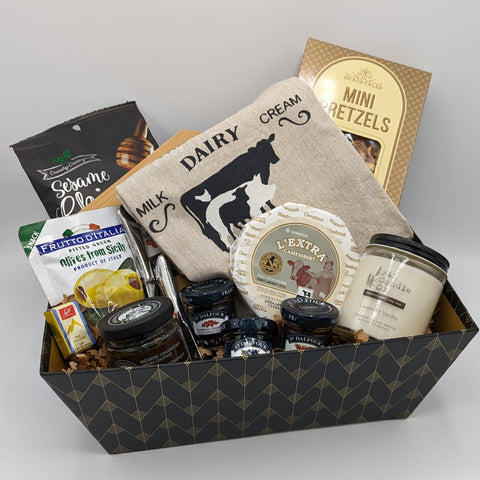 Happy Home Basket with a selection of products including charcuterie board and spreaders, jams and jellies, a candle, and kitchen towel.